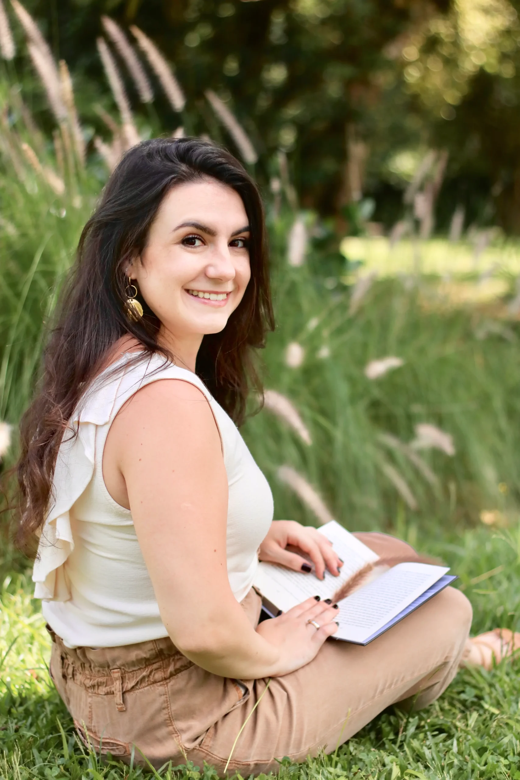 Ana Gabriela Bellaver, psicóloga, sorrindo ao ar livre com um livro nas mãos, representando clareza, leveza e conexão interior — princípios das mentorias para autoconhecimento, propósito e escolhas conscientes.