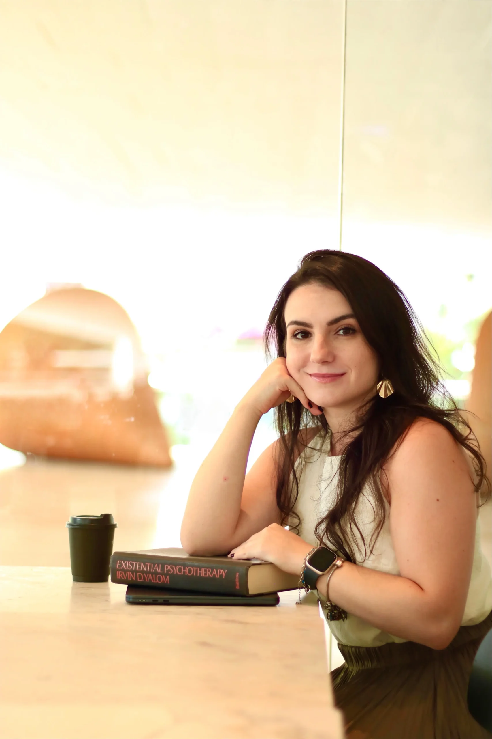 Psicóloga Ana Gabriela Bellaver sentada à mesa com o livro Existential Psychotherapy de Irvin D. Yalom, representando sua abordagem humanista-existencial na prática clínica.